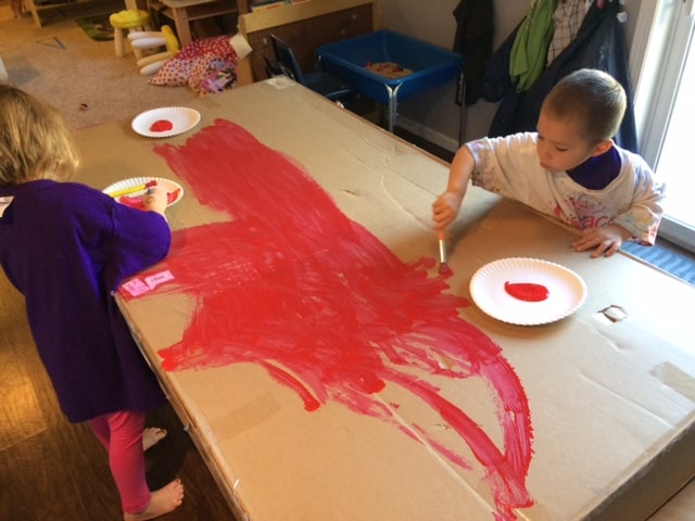 preschool boy painting red on a large piece of cardboard for fire safety activity