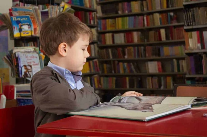 young boy reading a book in library