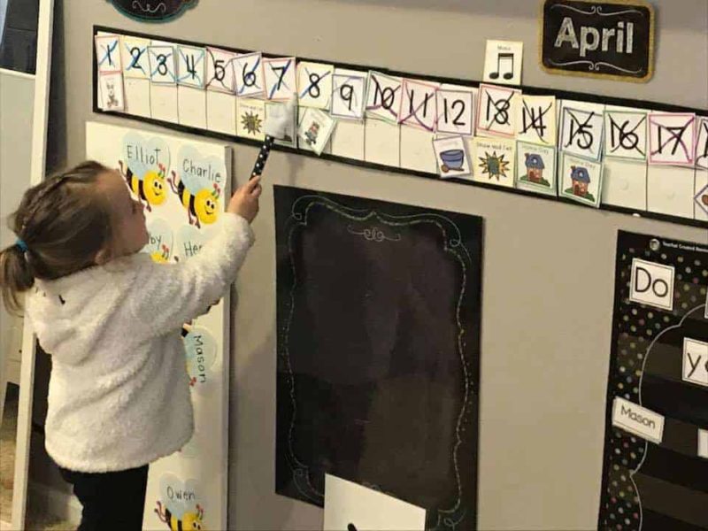 preschool girl wearing white sweatshirt pointing to numbers on the calendar with a wand