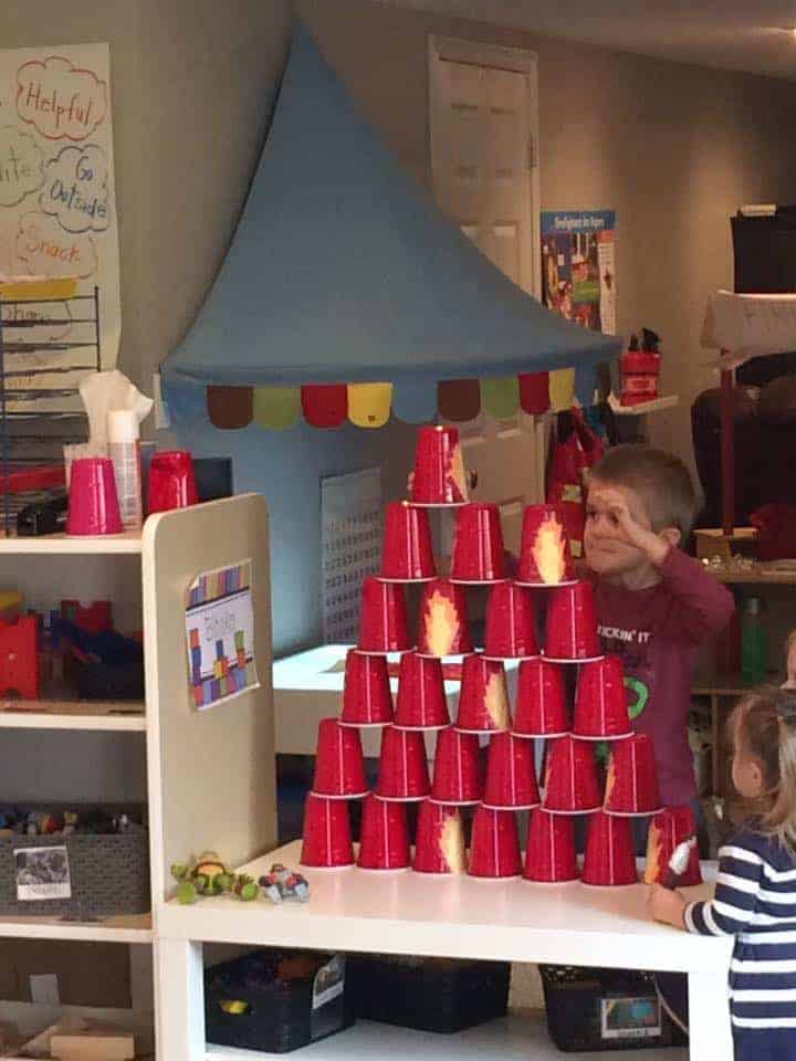 jongetje stapelt rode vuurbekers op elkaar om een toren te maken voor een wetenschappelijke activiteit over brandveiligheid