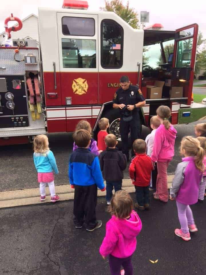 Bombero hablando con un grupo de niños pequeños frente al camión de bomberos