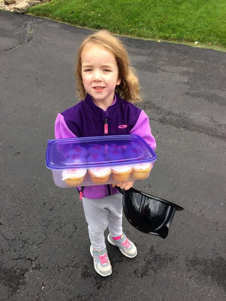 young girl carrying a container of cupcakes for