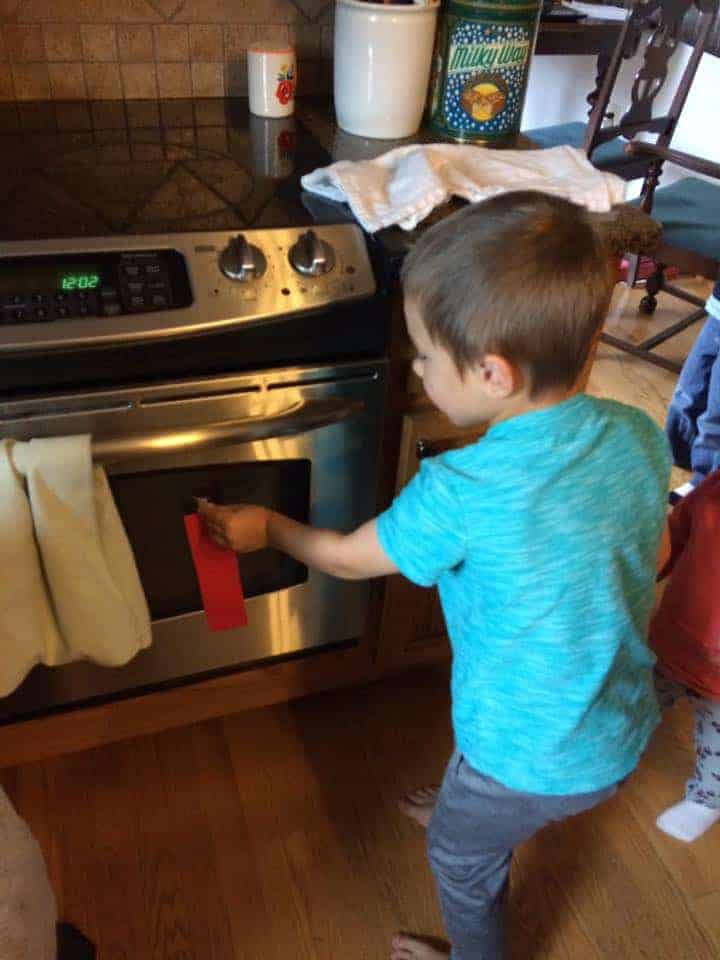 boy placing red paper strip on oven door fire safety activities