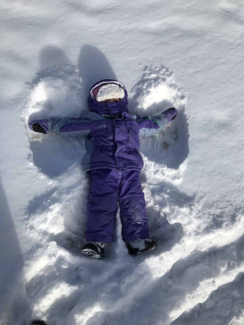 little girl in purple winter gear making snow angel