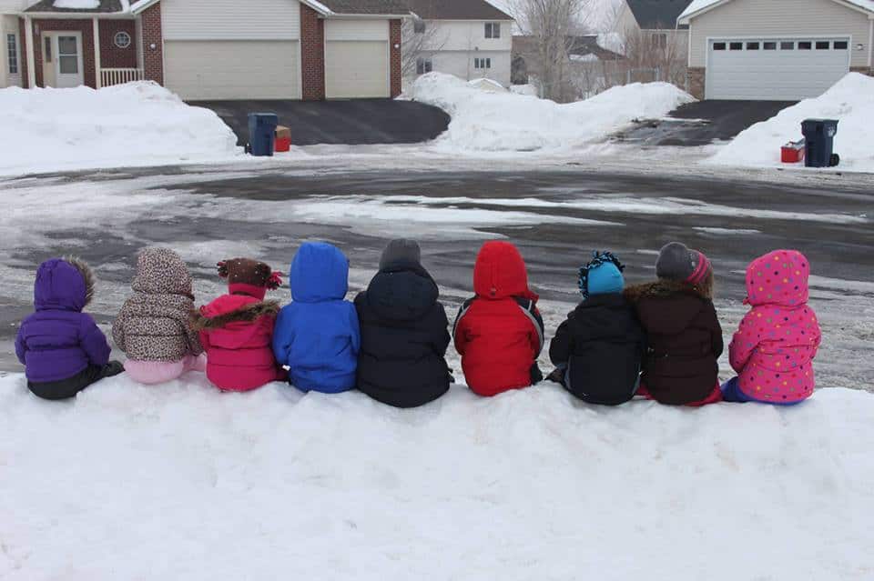 row of young kids sitting on snowbank in snow gear