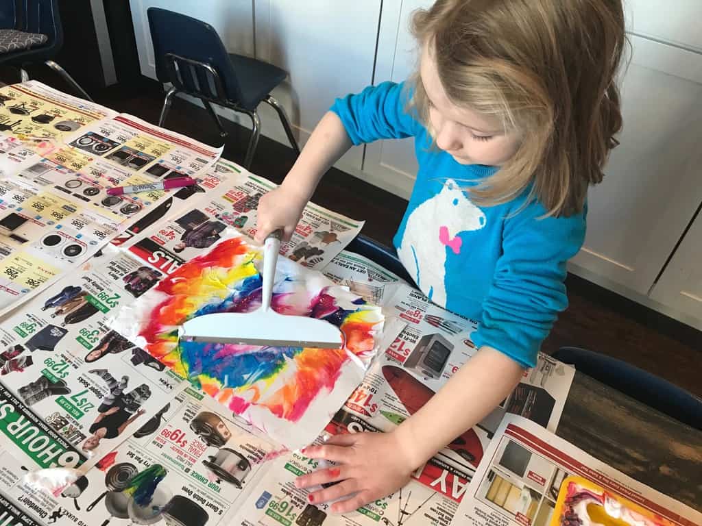 young girl using a squeegee on paint and paper