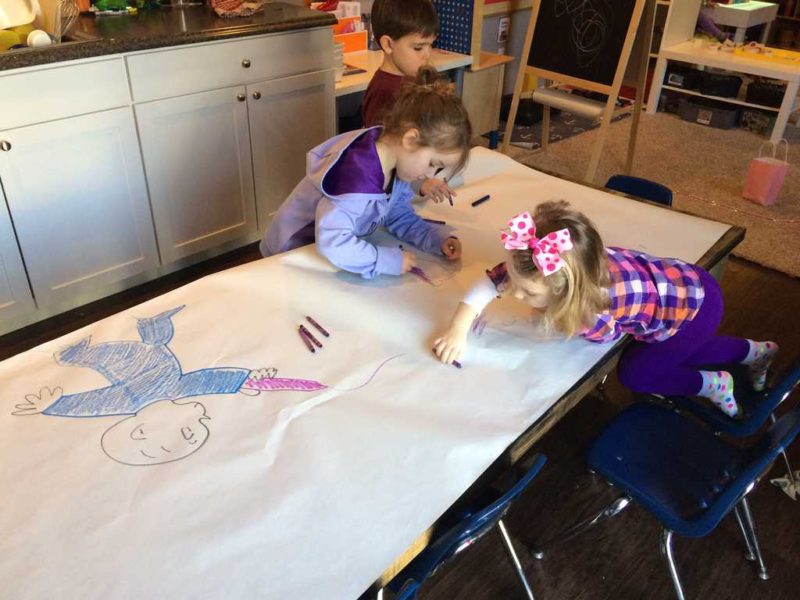 kids coloring on a large sheet of paper at the table