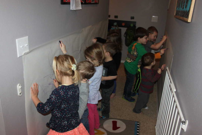 kids coloring with purple crayon on the wall