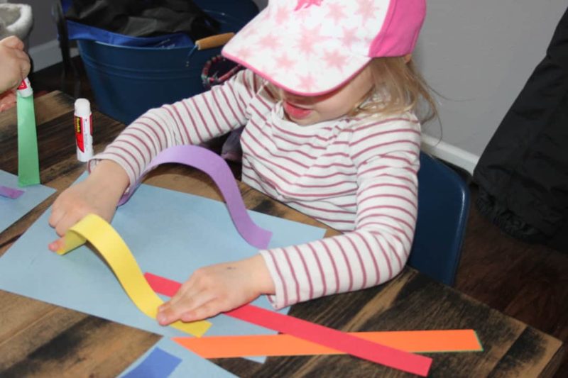 young girl gluing colorful strips to paper