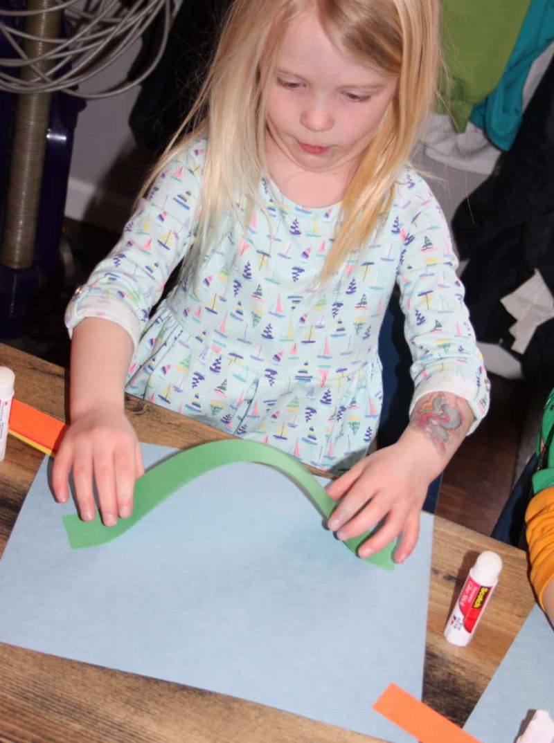 young girl glue green strip to paper