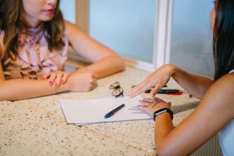 two woman at desk writing with paper and pen learning how to write child care contract together