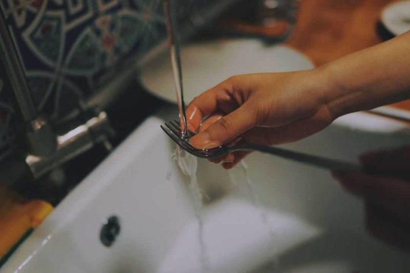 person washing a fork in the sink