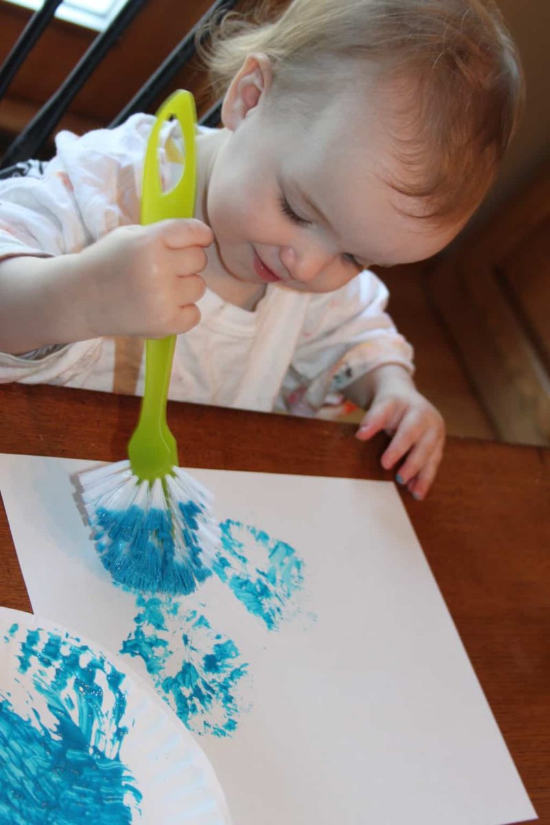 toddler girl painting with a blue scrub brush