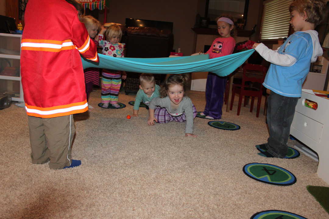 young children holding a sheet for other kids to crawl under 