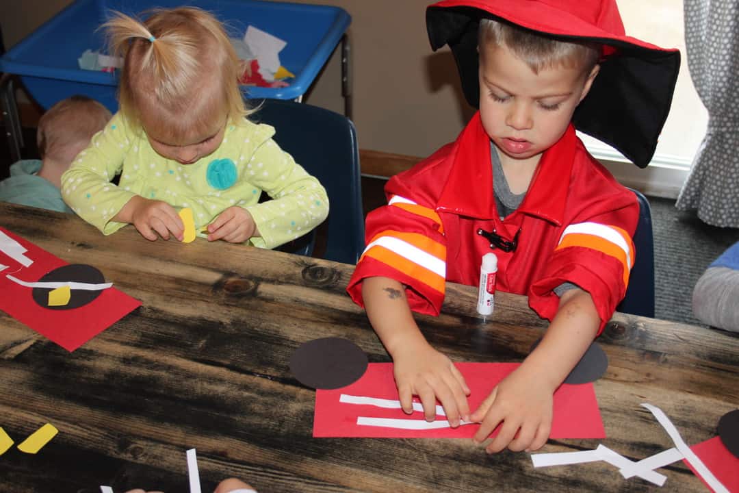 jeune en costume de pompier fabriquant un camion de pompier en papier pour un bricolage sur la sécurité incendie pour les enfants d'âge préscolaire