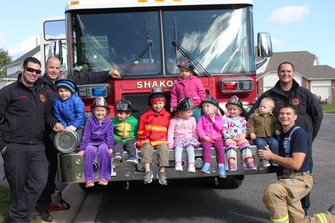 group of young kids sitting on fire truck with firefighters