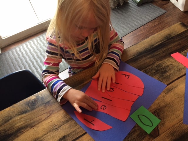 preschool girl gluing letters together to make a paper apple