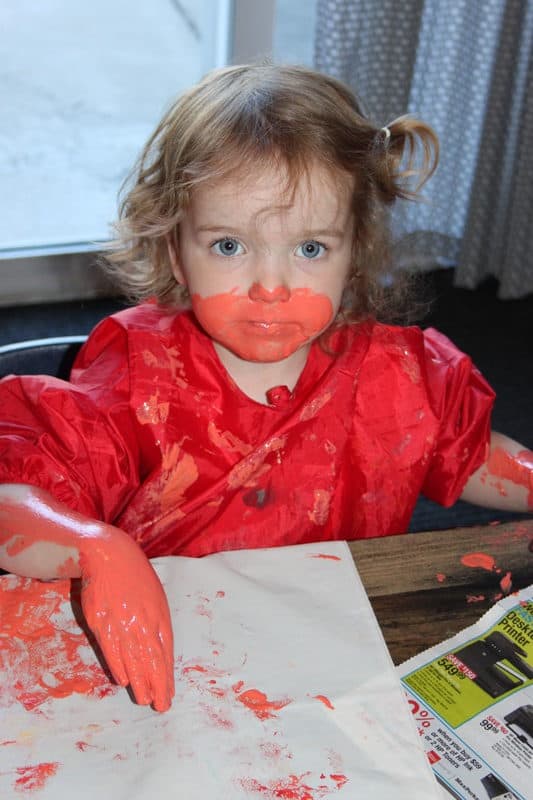 toddler girl covered in peach paint on hands and face