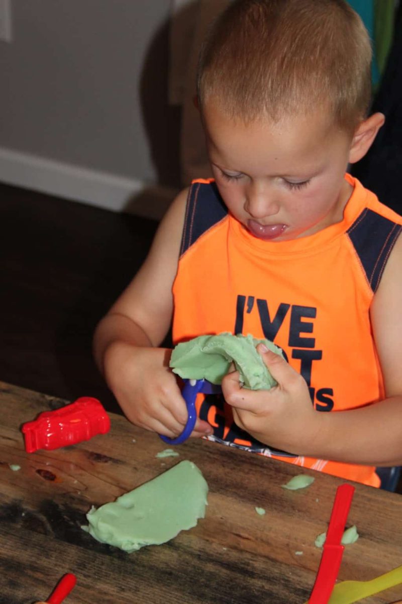 young boy cutting playdoh with scissors and sticking out tongue