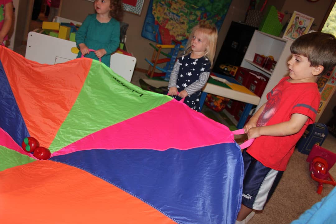 young kids holding a colorful parachute with plastic apples in the center