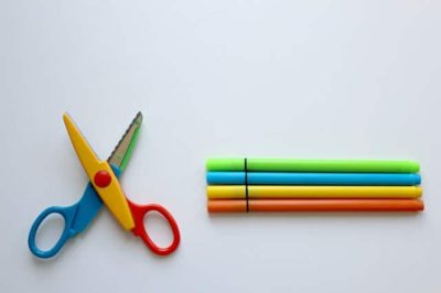 kid scissors lying open next to 4 colorful markers