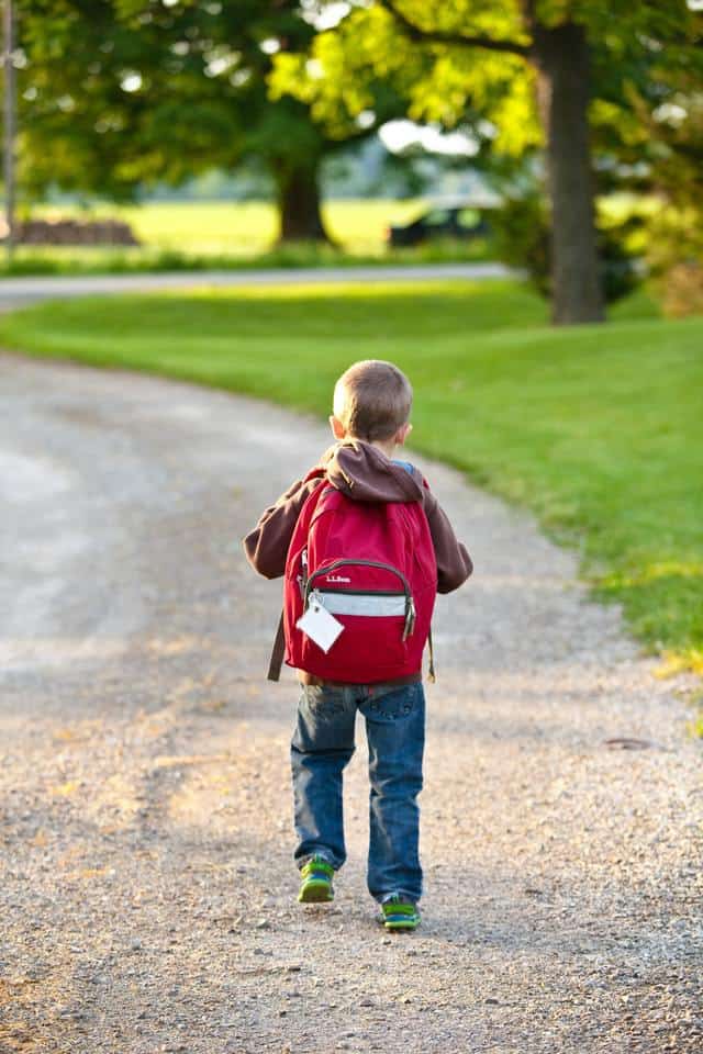 young boy walking down gravel path with a red backpack on his back