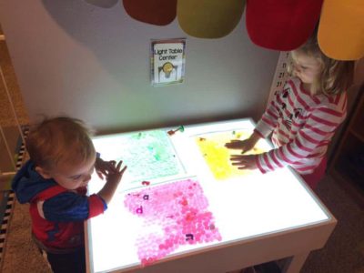 preschooler and toddler standing at light table with apple activity