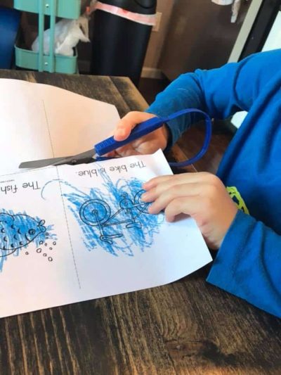 young child in blue shirt cutting paper with loop scissors