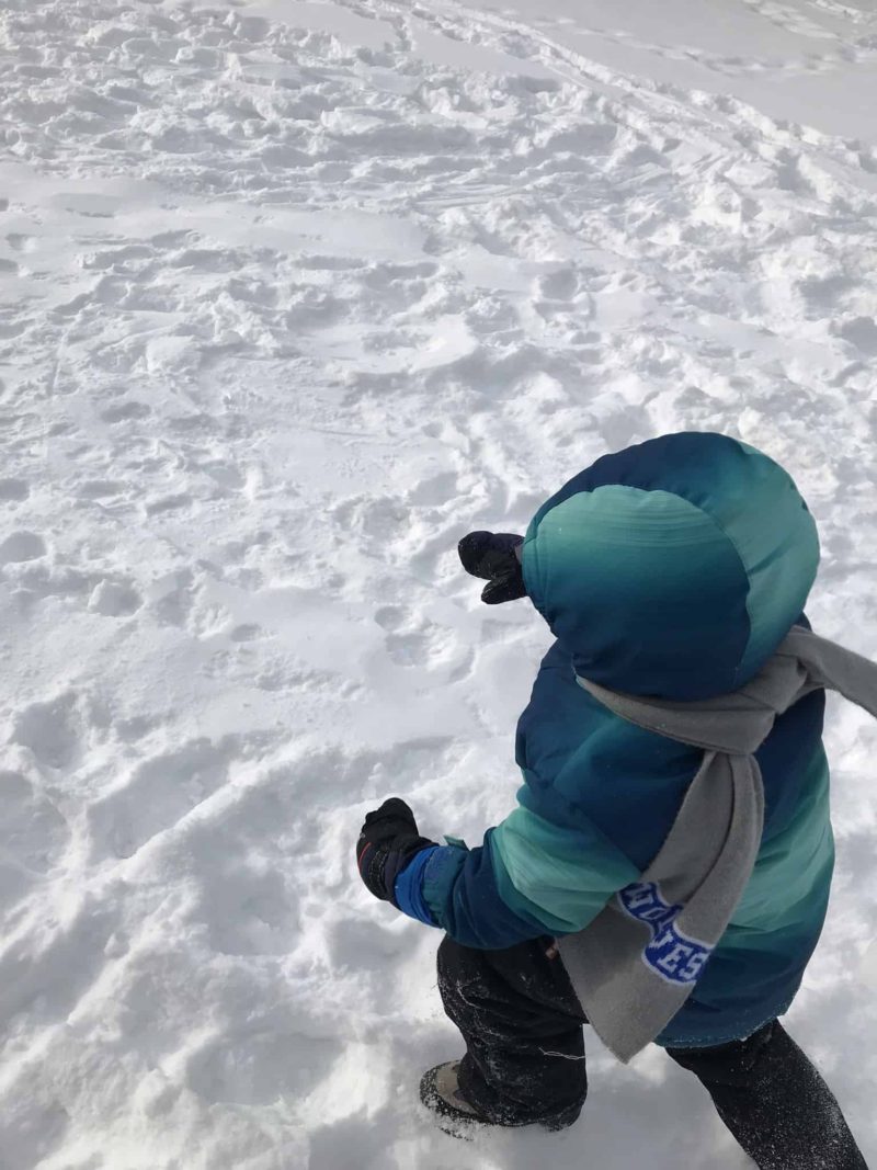 young boy wearing winter gear in family child care walking in snow